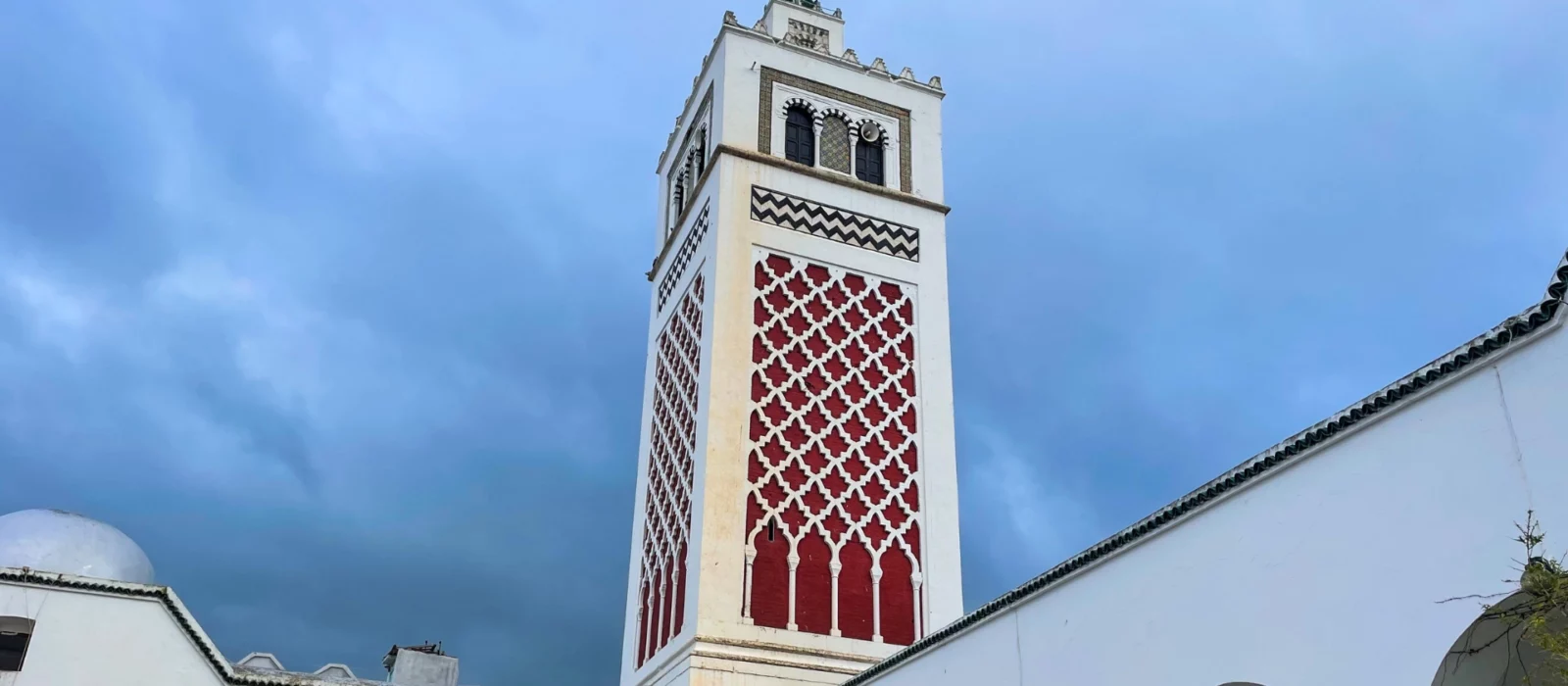 The minaret of the Great Mosque of Béja, a historic landmark in Tunisia, showcasing intricate Islamic architecture against a clear blue sky.