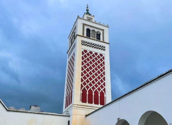 The minaret of the Great Mosque of Béja, a historic landmark in Tunisia, showcasing intricate Islamic architecture against a clear blue sky.