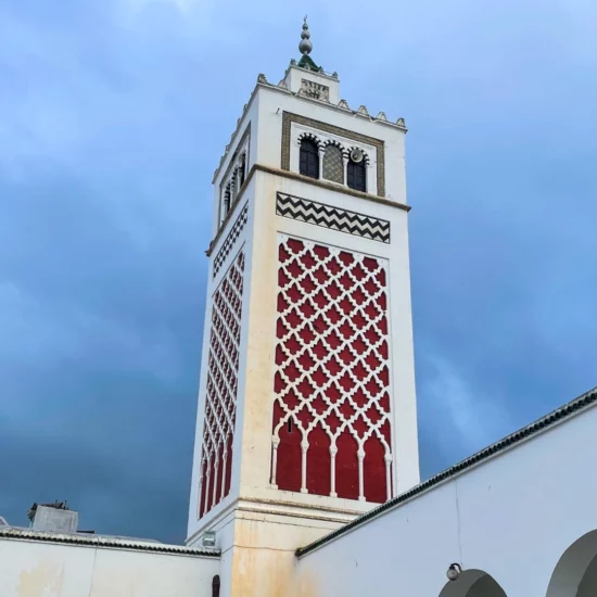 The minaret of the Great Mosque of Béja, a historic landmark in Tunisia, showcasing intricate Islamic architecture against a clear blue sky.