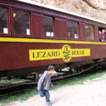 The Lezard Rouge train with its red lacquered carriages passing through the rocky Selja Gorges in Tunisia.