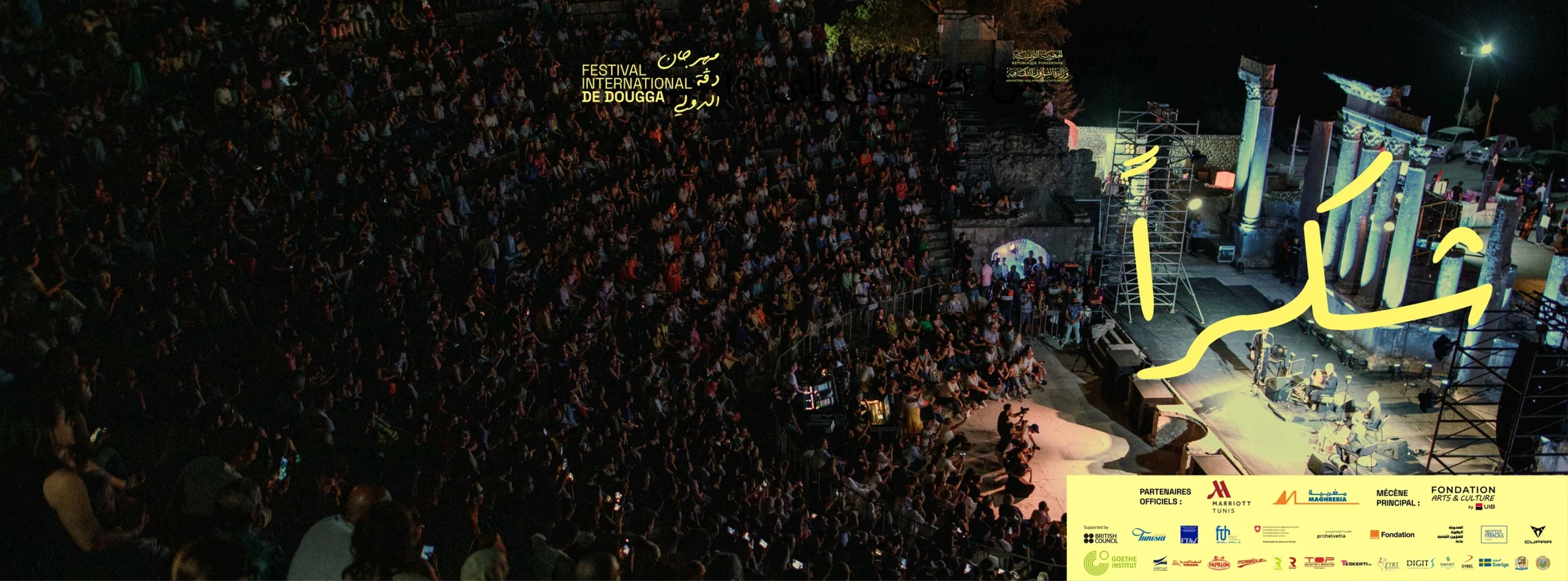 Ancient Roman Theatre of Dougga illuminated for the 2025 Festival, showing attendees during a performance.